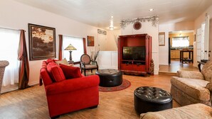 A living room with a red sofa, black ottoman, and a television on a wooden stand. - Sam Houston's Retreat | Walking distance to Festivals | Close to Main Street (Fredricksburg)