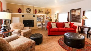 A living room with a fireplace, a red sofa, patterned armchairs, a bookshelf, and a painting on the wall. - Sam Houston's Retreat | Walking distance to Festivals | Close to Main Street (Fredricksburg)