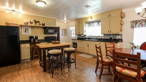 A compact kitchen with wooden flooring, a dining area with a wooden table and chairs, and a black refrigerator. - Sam Houston's Retreat | Walking distance to Festivals | Close to Main Street (Fredricksburg)