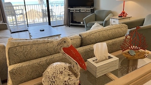 Una sala de estar con un ventanal grande, un televisor de pantalla plana, un sofá, una mesa de centro y una pieza decorativa con forma de tortuga marina.