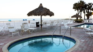 Zona de piscina con sillas de descanso y una sombrilla de paja, con vistas a la playa.