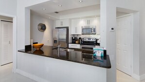 A modern kitchen with white cabinets, a stainless steel refrigerator, a microwave, and a large island with a sink. - One in a Minion themed condo, 5 mins to Disney | WiFi + Keurig (Kissimmee)