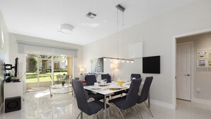 A modern dining area with a glass table, dark chairs, and a white ceiling. - One in a Minion themed condo, 5 mins to Disney | WiFi + Keurig (Kissimmee)