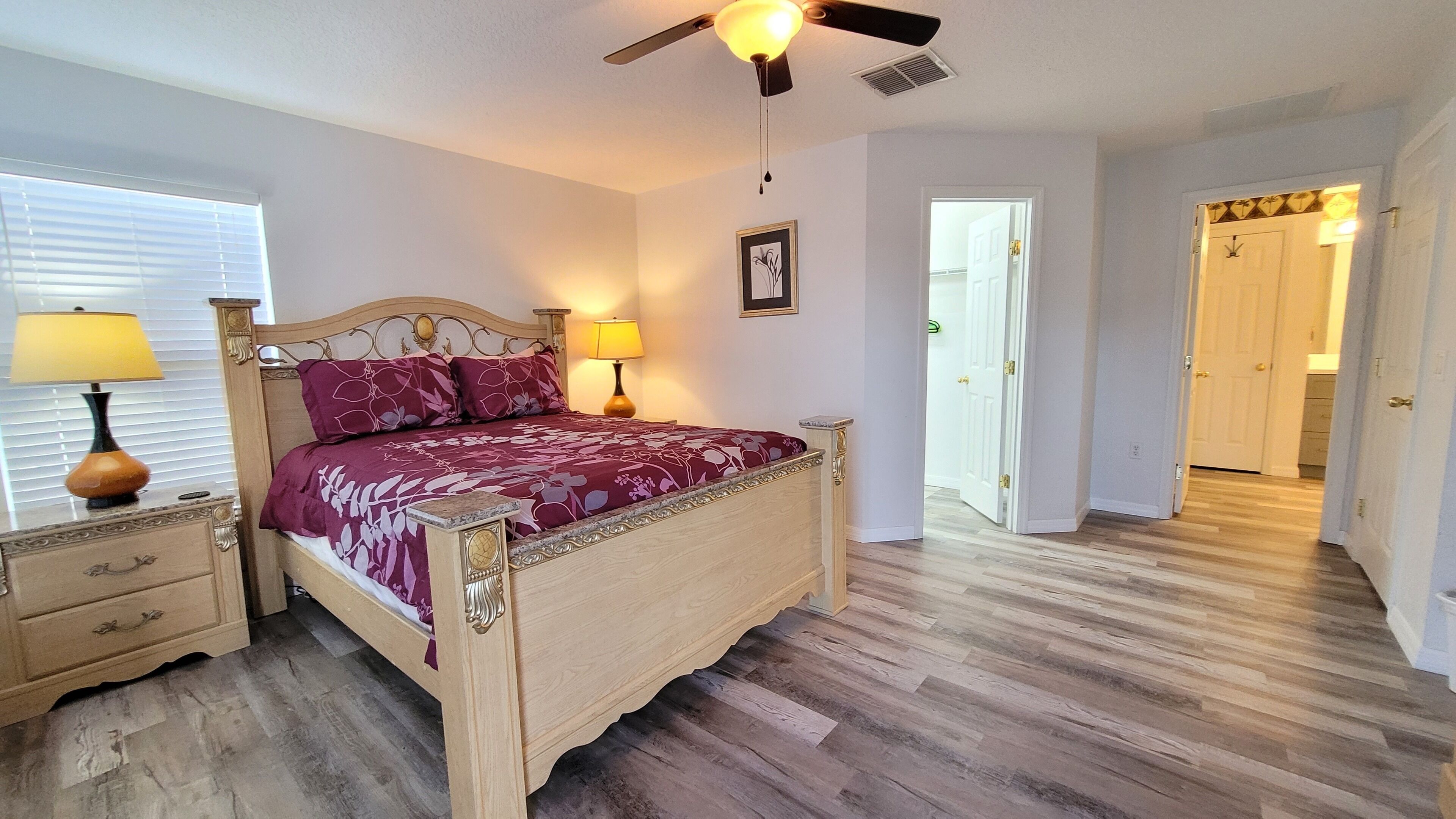 A bedroom with a wooden bed, two bedside tables with lamps, a ceiling fan, and a framed picture on the wall.