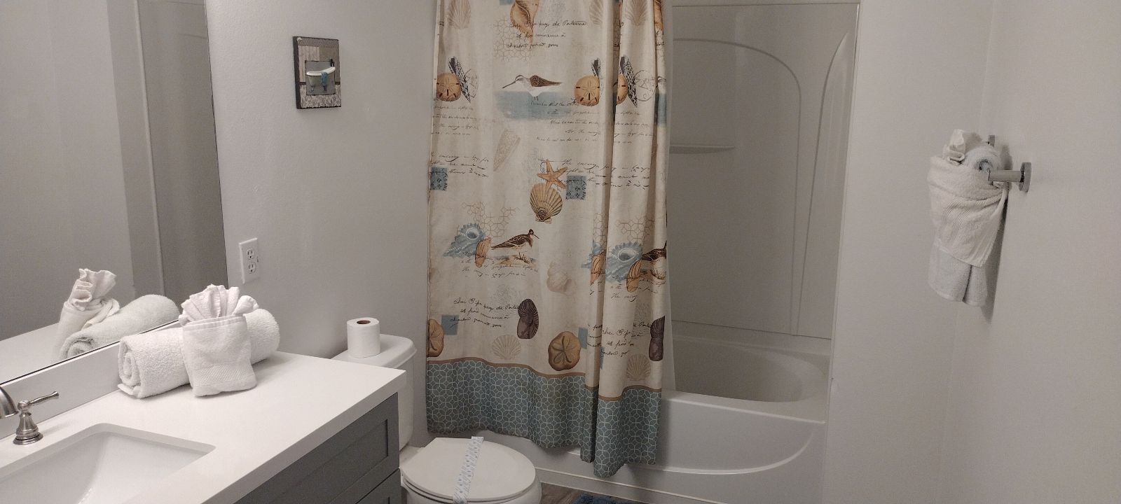 A bathroom with a sink, toilet, and bathtub. There are towels and a shower curtain with a nautical theme.