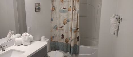 A bathroom with a sink, toilet, and bathtub. There are towels and a shower curtain with a nautical theme.