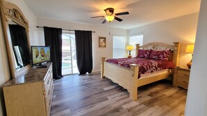 Un dormitorio con cama de madera, ventilador de techo, televisor y vistas al exterior.