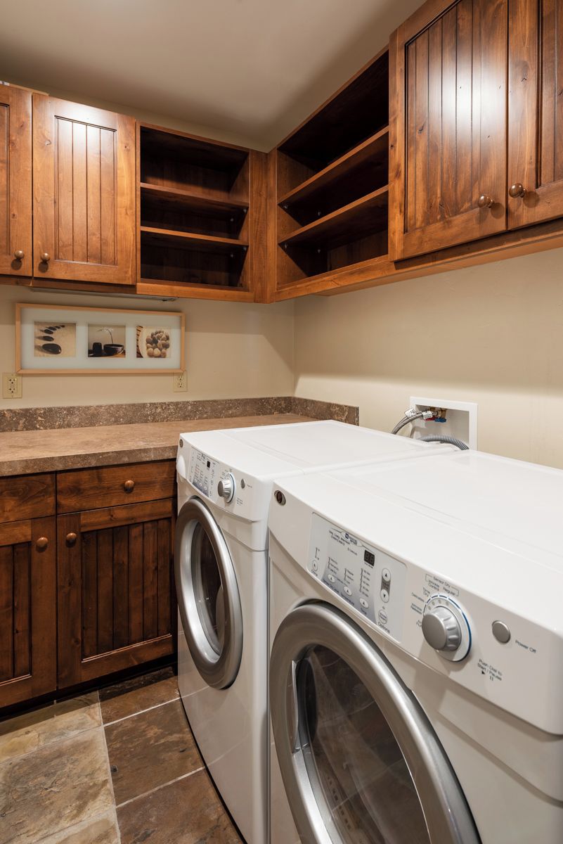 Un espace buanderie équipé d’un lave-linge à chargement frontal, de meubles en bois et d’un plan de travail en marbre.
