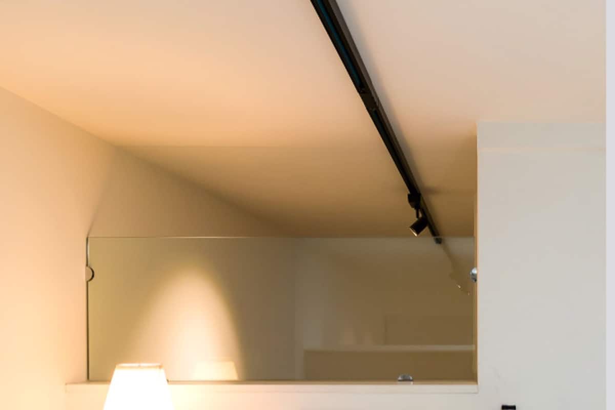 Une chambre d’hôtel comprenant un lit, une table de chevet, une lampe, un miroir et un luminaire au plafond.