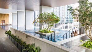 Une piscine intérieure offrant une vue sur le paysage urbain, entourée de plantes et d’une architecture moderne.