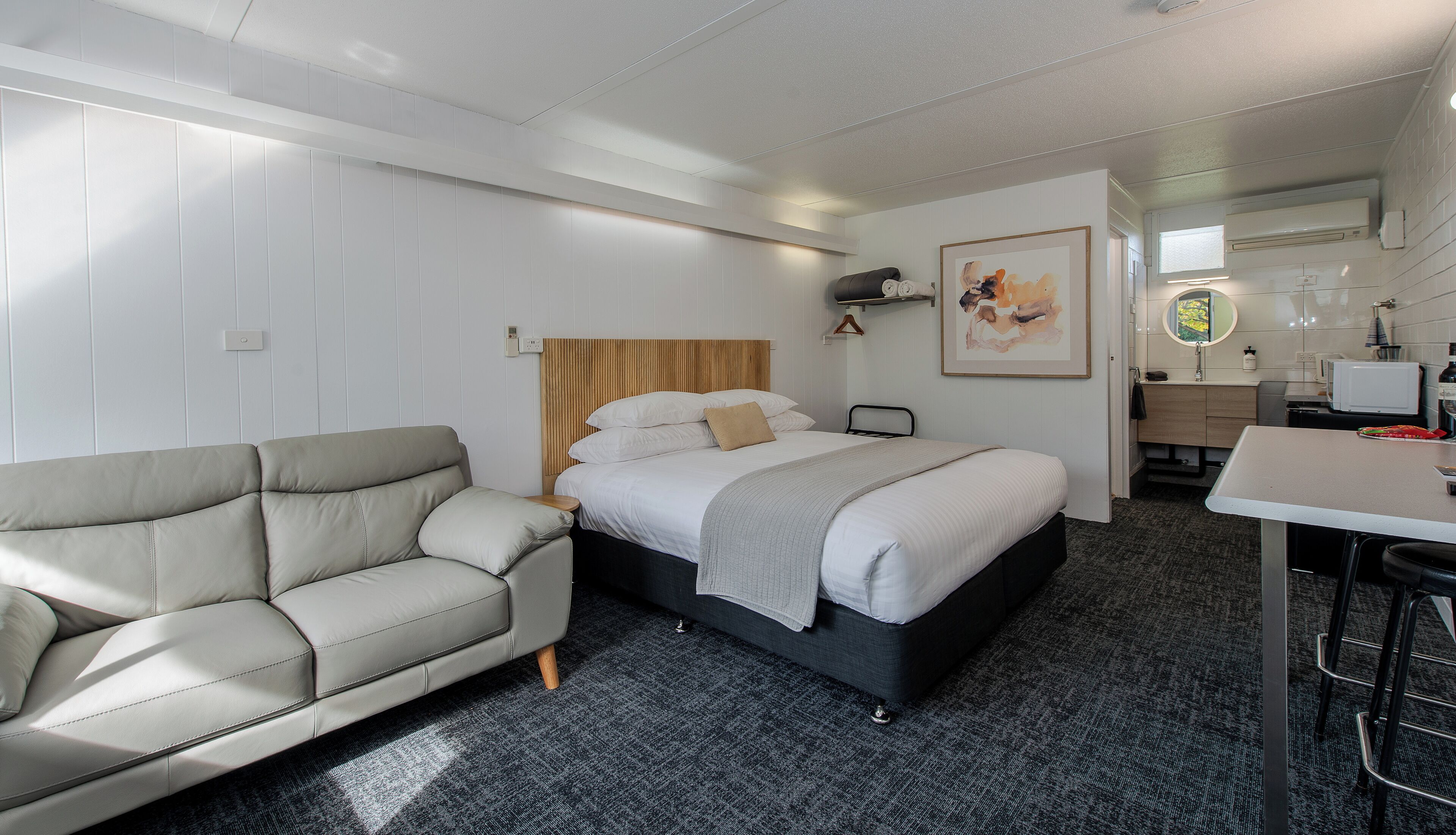 A modern hotel room with a bed, a sofa, a desk, and a bathroom.