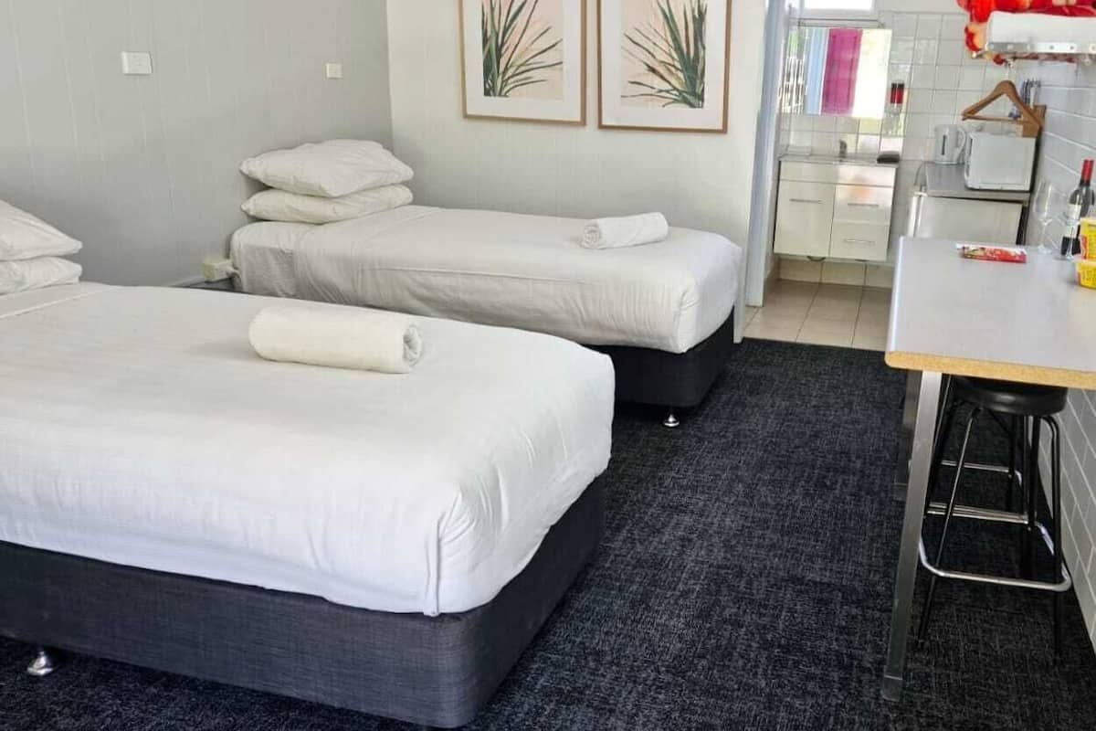 A hotel room with two beds, a kitchenette, and a small dining area.