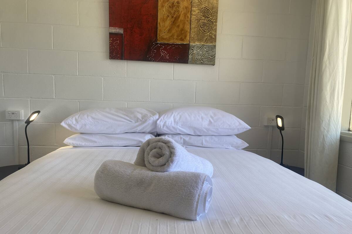A neatly made bed with white linens, a rolled towel, and two bedside lamps.