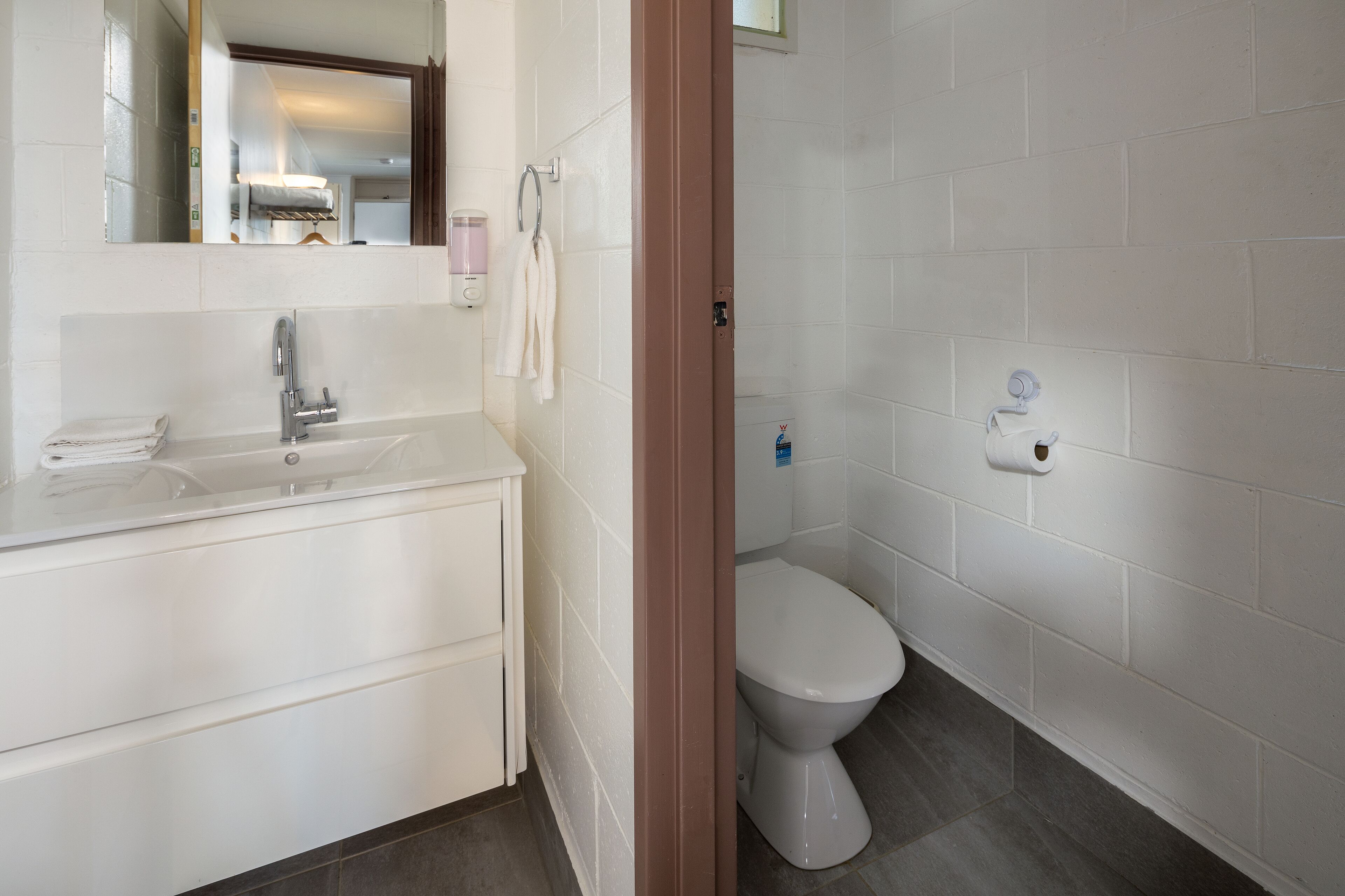 Un baño con lavamanos, espejo y retrete blancos.