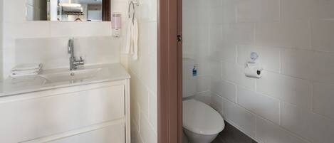 Un baño con lavamanos, espejo y retrete blancos.