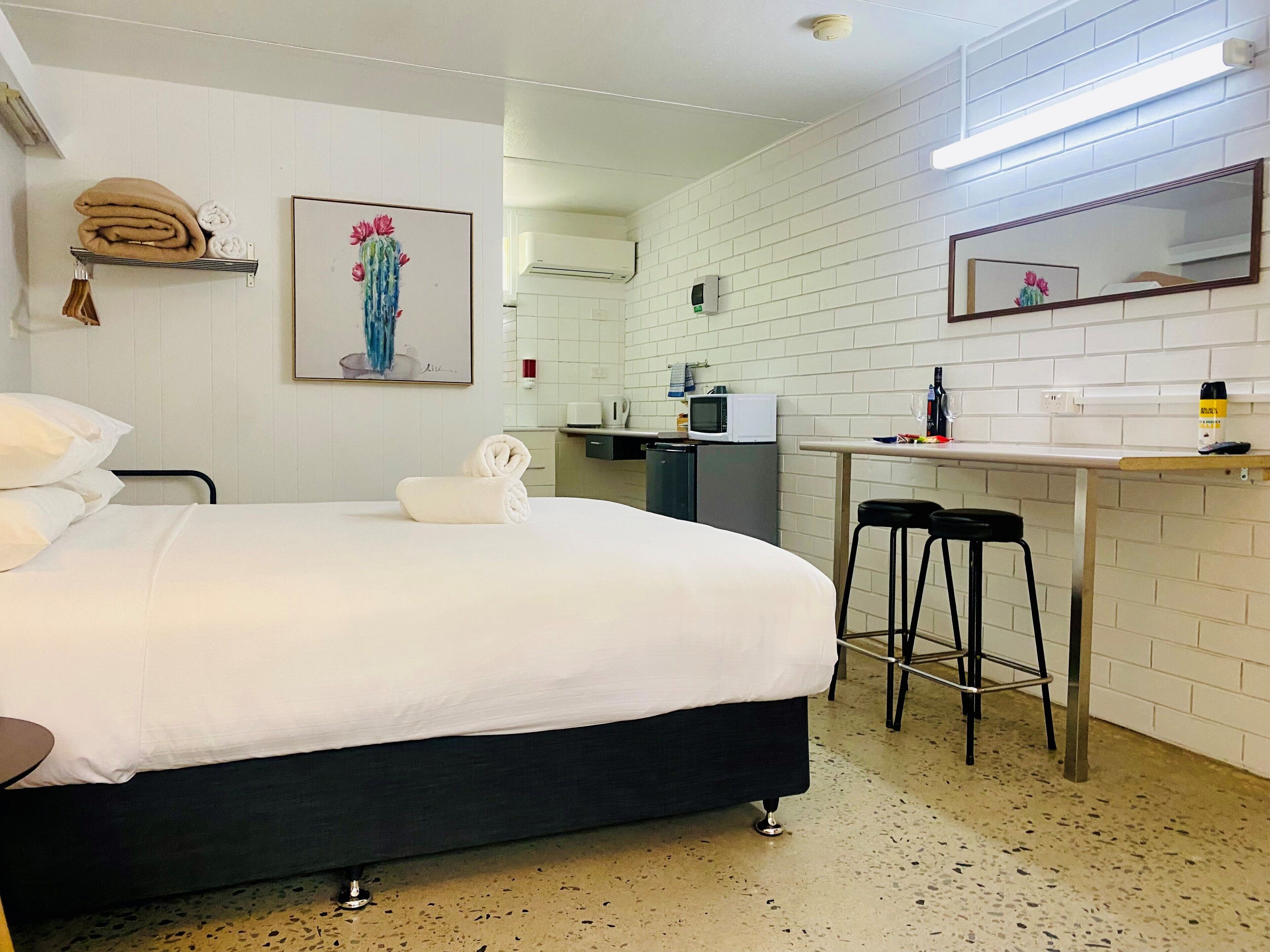 A hotel room with a bed, a desk, a chair, a microwave, a refrigerator, and a sink.