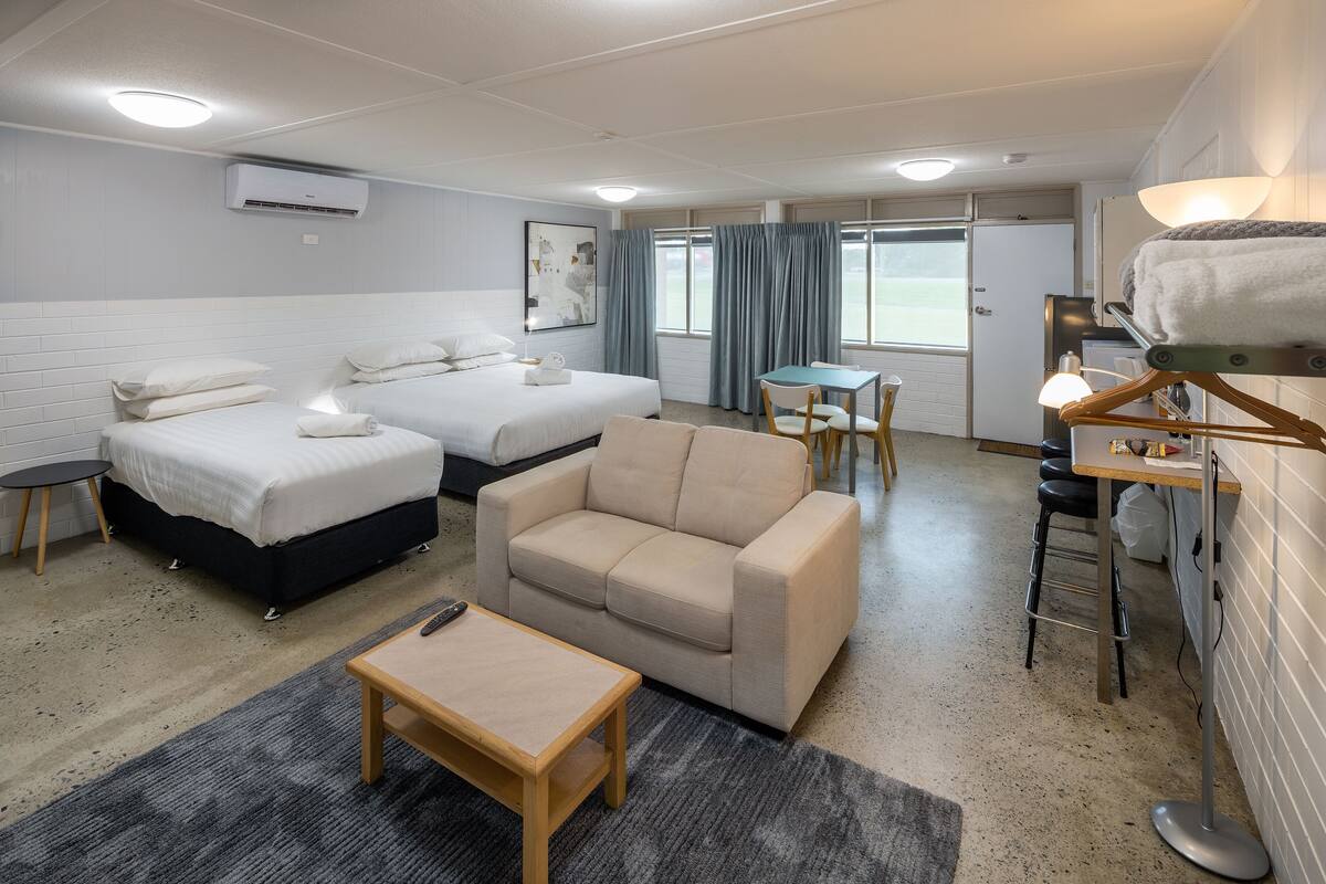 A hotel room with two beds, a sofa, a small table, a chair, a desk, and a lamp.