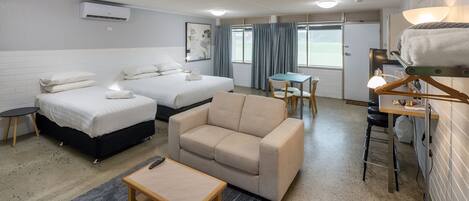 Habitación de hotel con dos camas, un sofá, una mesita, una silla, un escritorio y una lámpara.