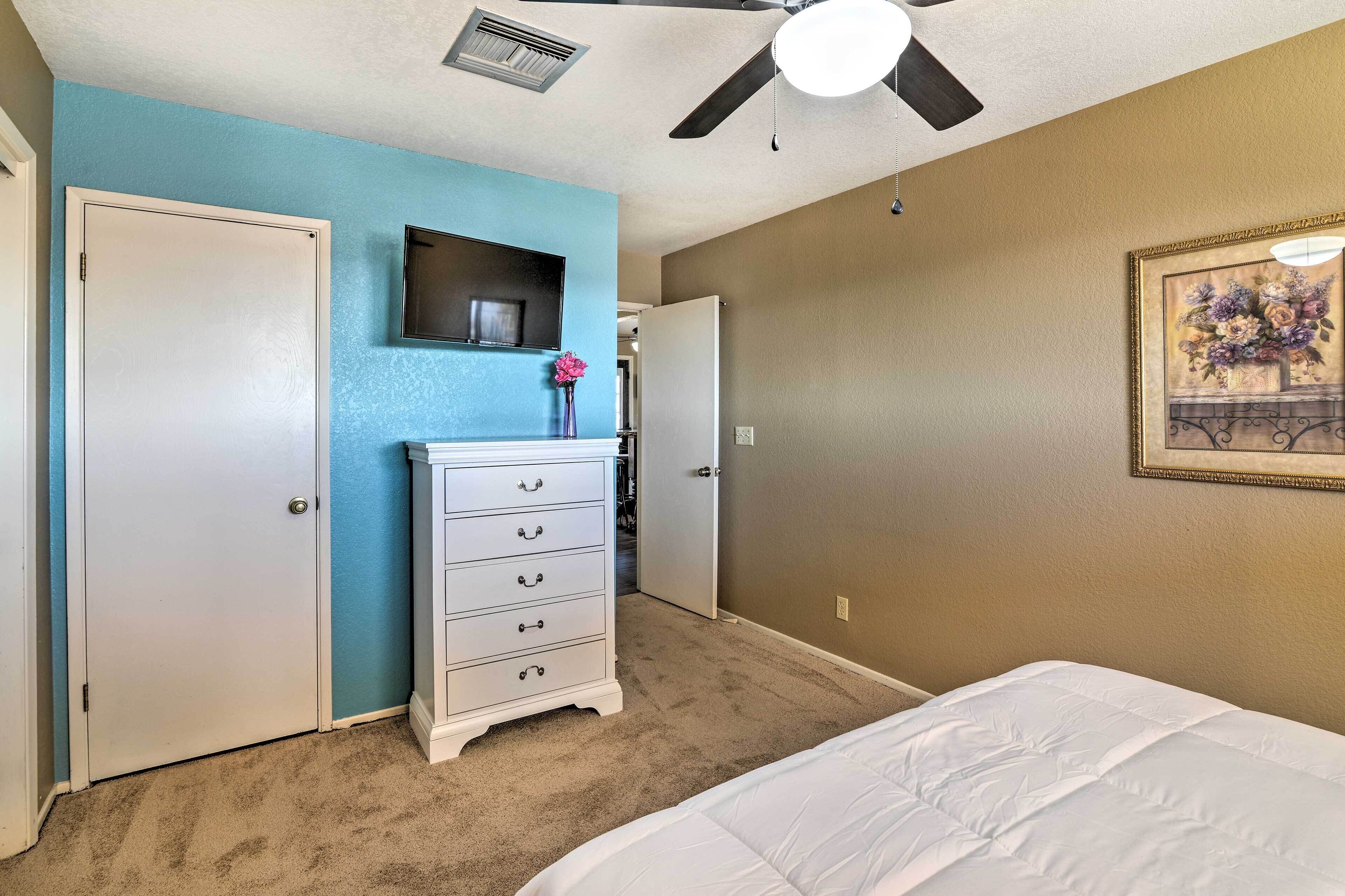 A bedroom with a bed, a dresser, a television mounted on the wall, and a ceiling fan.