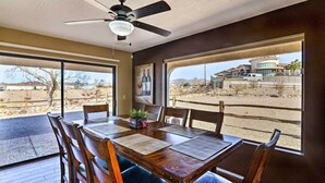 A dining area with a table and chairs, a ceiling fan, and large windows with a view of a desert landscape and a building.
