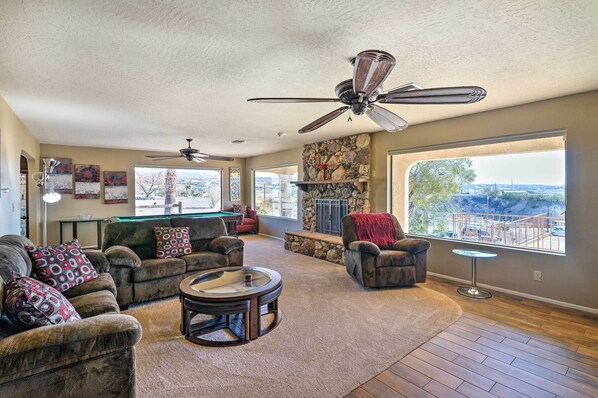 A spacious living room with a pool table, comfortable seating, a fireplace, and a large window offering a scenic view.