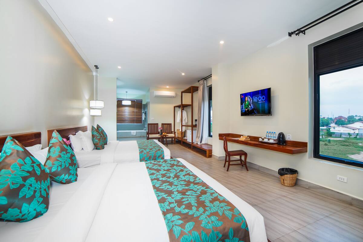 A hotel room with a large bed, a desk, a TV, and a view of the outside.