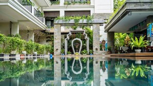 A serene indoor pool with a central statue, surrounded by lush greenery and a modern building facade. - Bayon Modern Residence (Siem Reap)