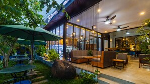 An outdoor seating area with tables and chairs, a large rock, and a staircase leading to an upper level. - Bayon Modern Residence (Siem Reap)