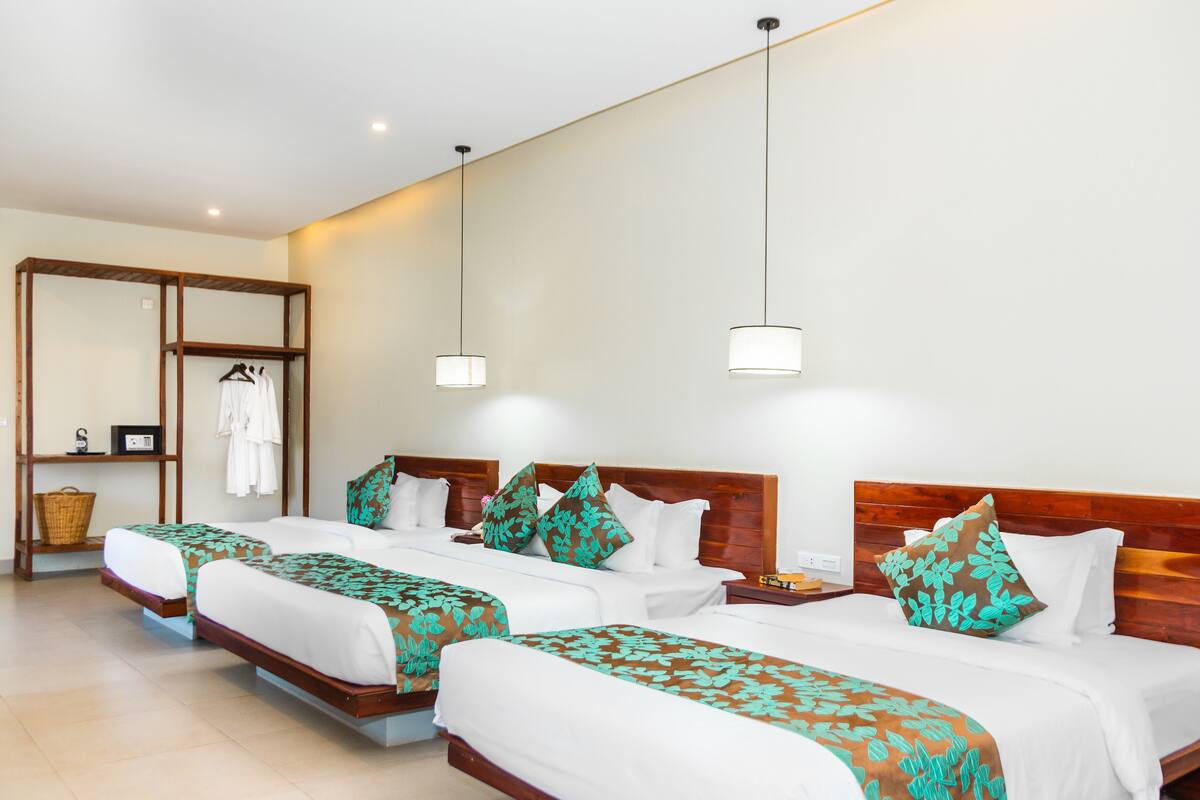 A hotel room with three beds, a wooden headboard, a hanging light fixture, and a small table with a basket and a radio.