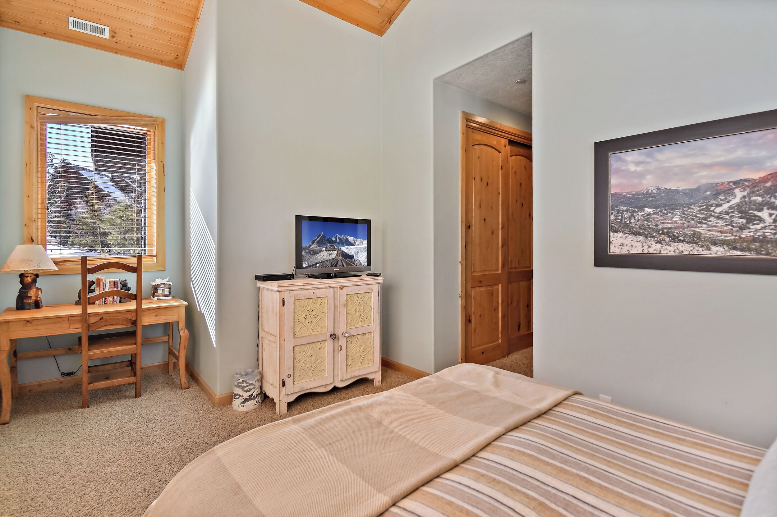 A bedroom with a bed, a desk with a chair, a television, and a wardrobe.