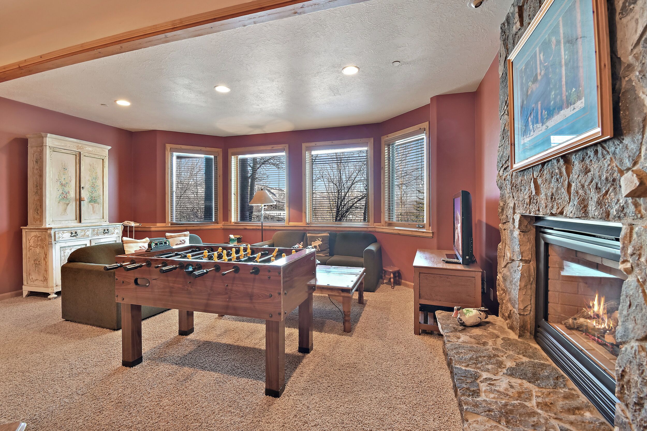 A cozy room with a foosball table, a fireplace, and large windows.