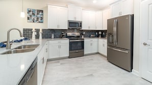 A modern kitchen with white cabinets, stainless steel appliances, and a tiled backsplash.