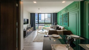 A modern living room with a dining area, a sofa, a coffee table, and a view of the city through large windows. - Maven Stylish Hotel Bangkok (Bangkok)