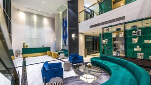 A modern lobby with green and blue seating, marble flooring, and a glass display of decorative items. - Maven Stylish Hotel Bangkok (Bangkok)