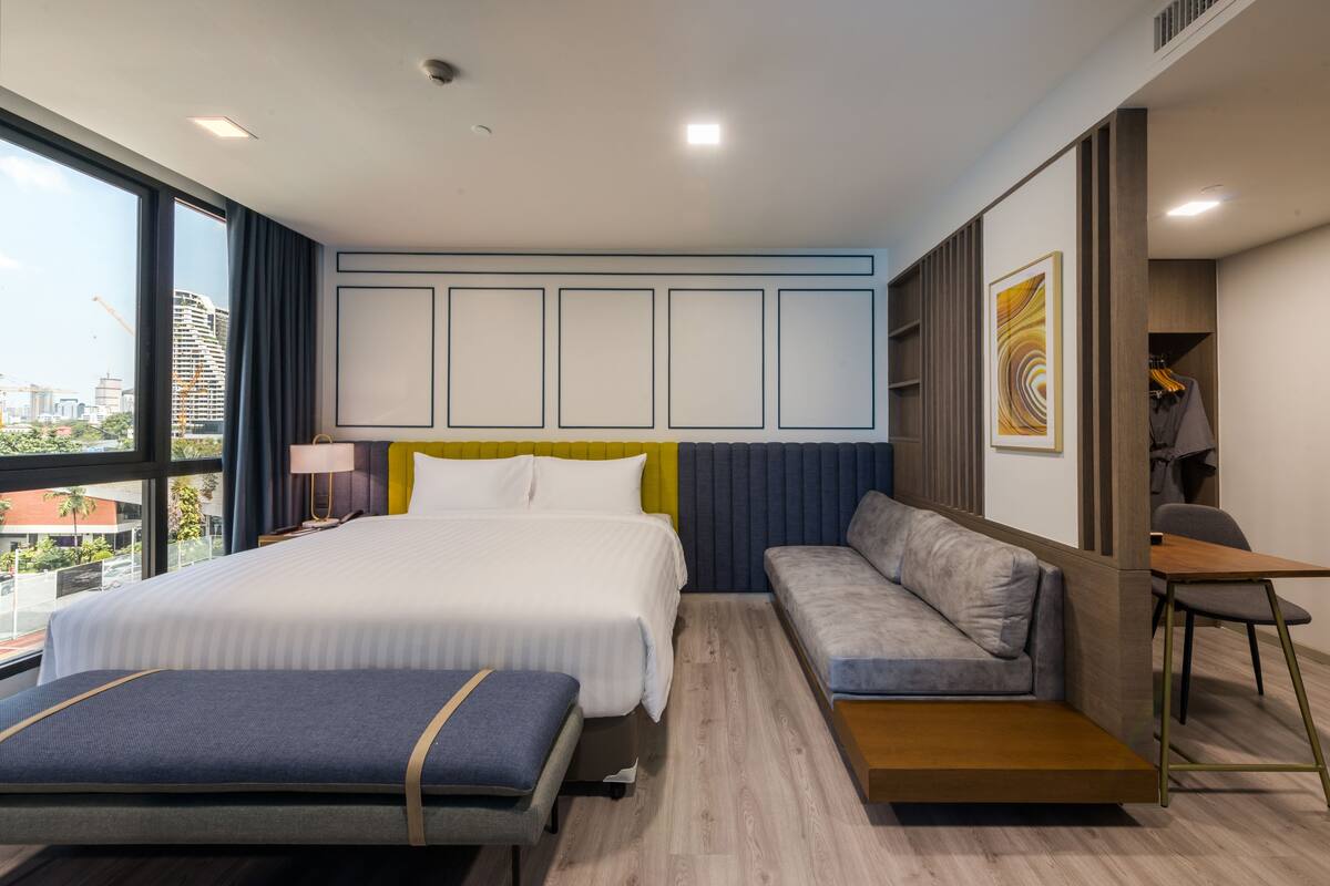Ein modernes Hotelzimmer mit einem großen Bett, einer Couch, einem Schreibtisch und Blick auf die Stadt.