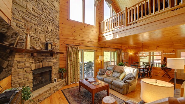 A spacious living room with a stone fireplace, wooden floors, a high ceiling, and a balcony. - Maggie Valley Cabin w/ Private Hot Tub & Game Room (Maggie Valley)
