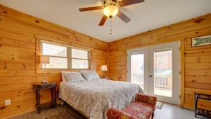A wooden cabin bedroom with a bed, bedside tables, a bench, and a ceiling fan. - Maggie Valley Cabin w/ Private Hot Tub & Game Room (Maggie Valley)