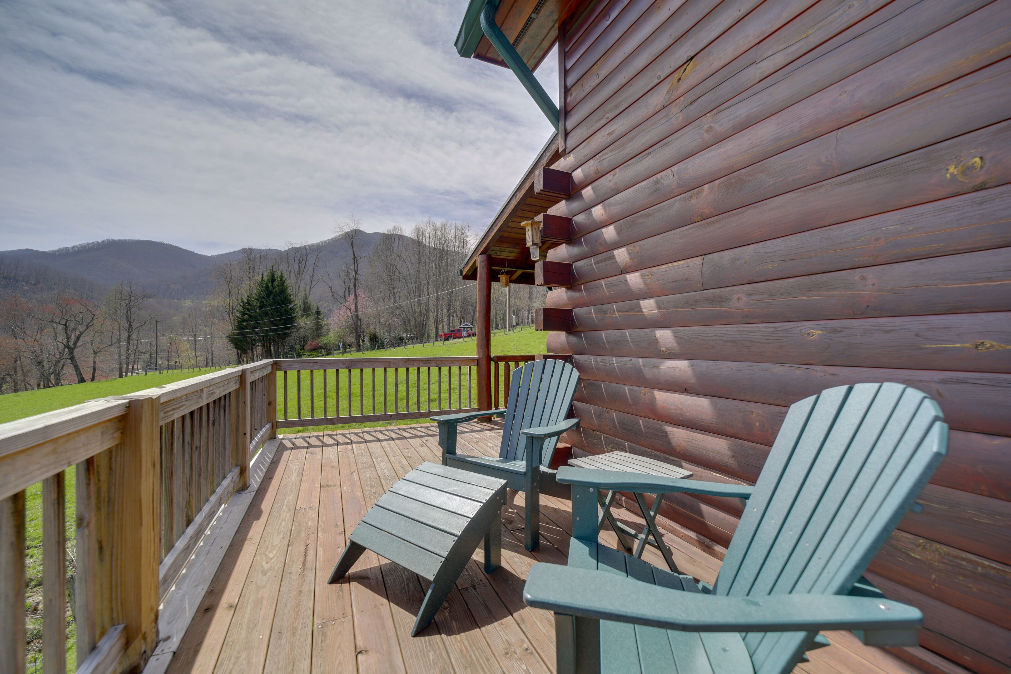 A wooden deck with Adirondack chairs, a wooden railing, and a mountain view.