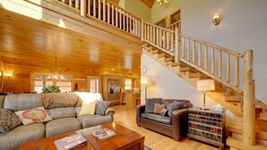 A spacious living area with a wooden staircase, leather sofas, and a coffee table. - Maggie Valley Cabin w/ Private Hot Tub & Game Room (Maggie Valley)