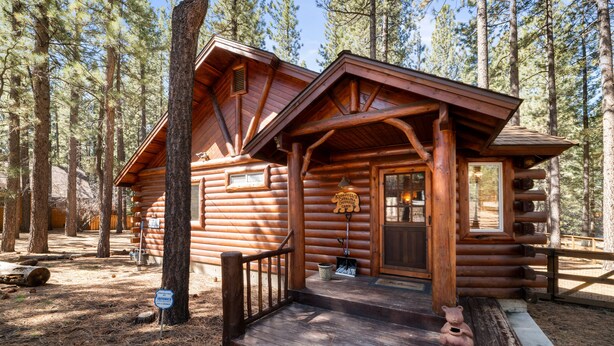 A log cabin with a wooden porch, a front door, and a window. - Catalina Creekside Cabin - Log Cabin, Perfect for Couples, Fenced Yard (Big Bear Lake)