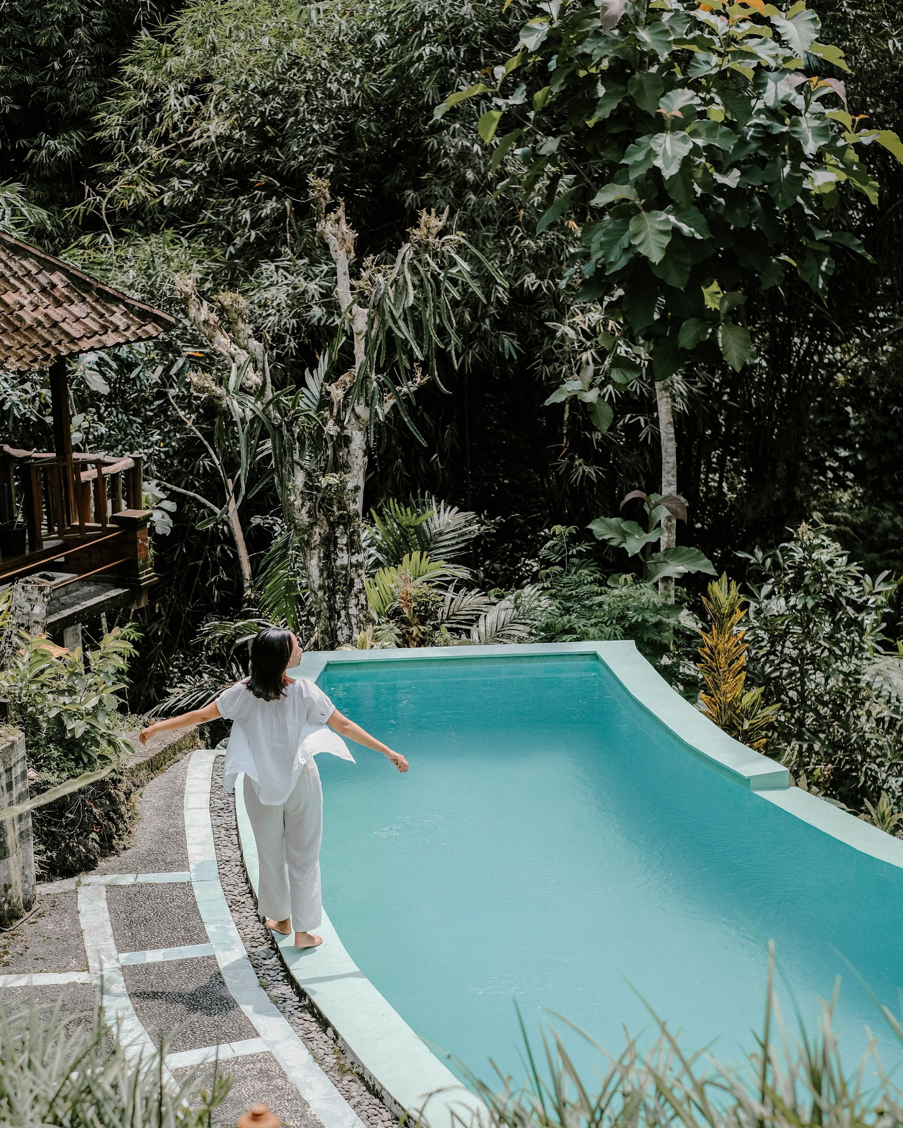 A person walking along a curved pool edge surrounded by lush greenery.