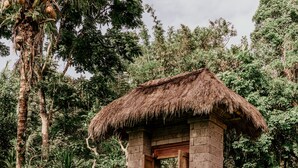 A rustic hut with a thatched roof, surrounded by lush greenery and a stone wall. - Song Broek Jungle Resort (Payangan)