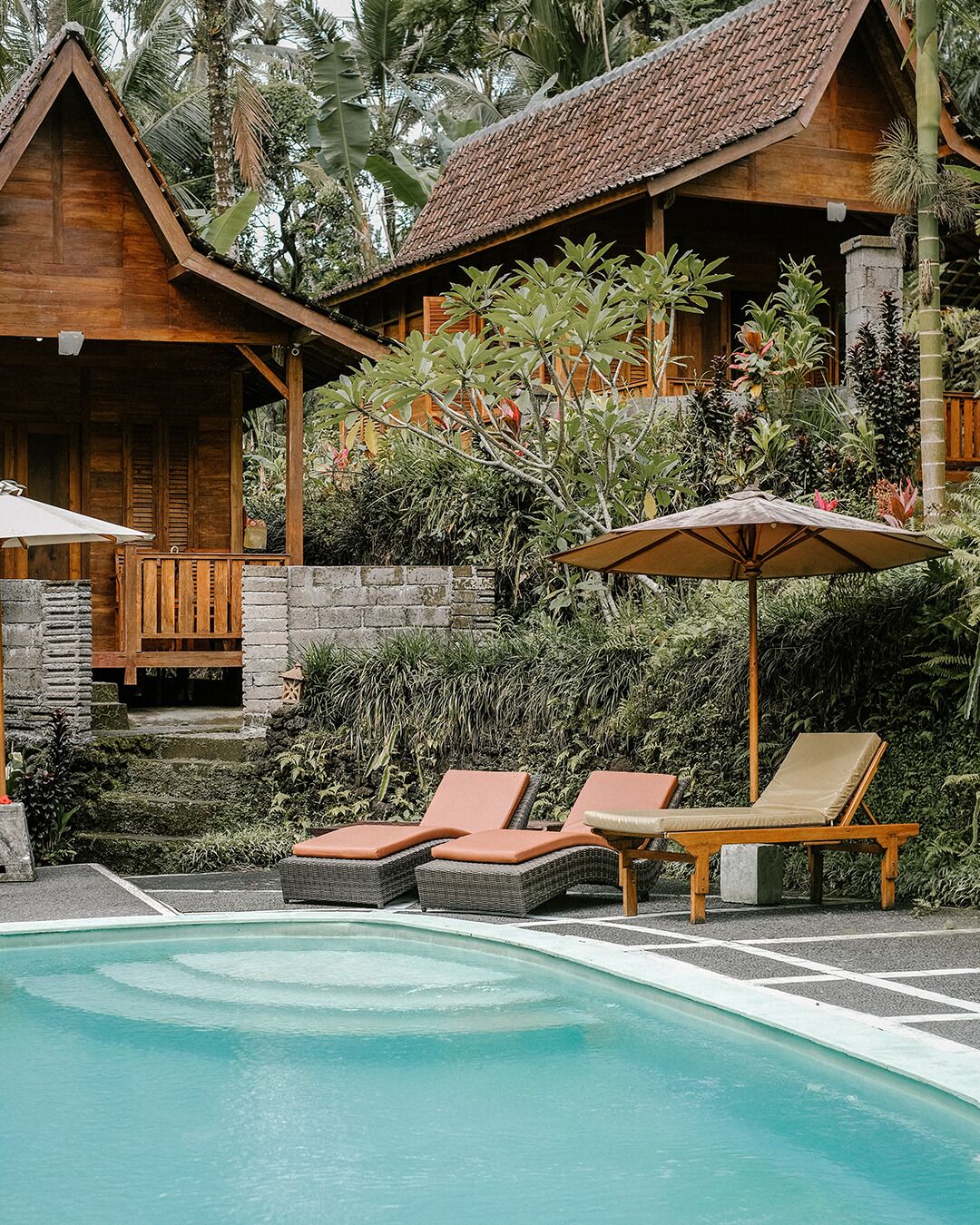 Zona de piscina con sillones reclinables y un edificio de madera con techo de tejas.