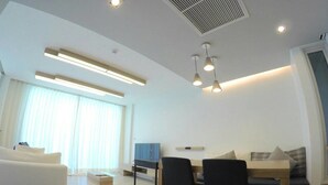 A modern living room with a sofa, a dining table with chairs, a TV, and a large window with curtains. - Luxury Wanvayla Condo (Hua Hin)