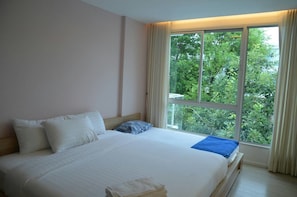 A hotel room with a large bed, a window with curtains, and a view of greenery outside.
