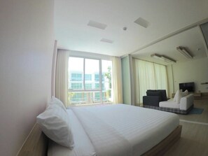 A hotel room with a large bed, a sofa, a TV, and a balcony with curtains.