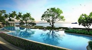 A swimming pool with a view of the sea, surrounded by palm trees and a building.