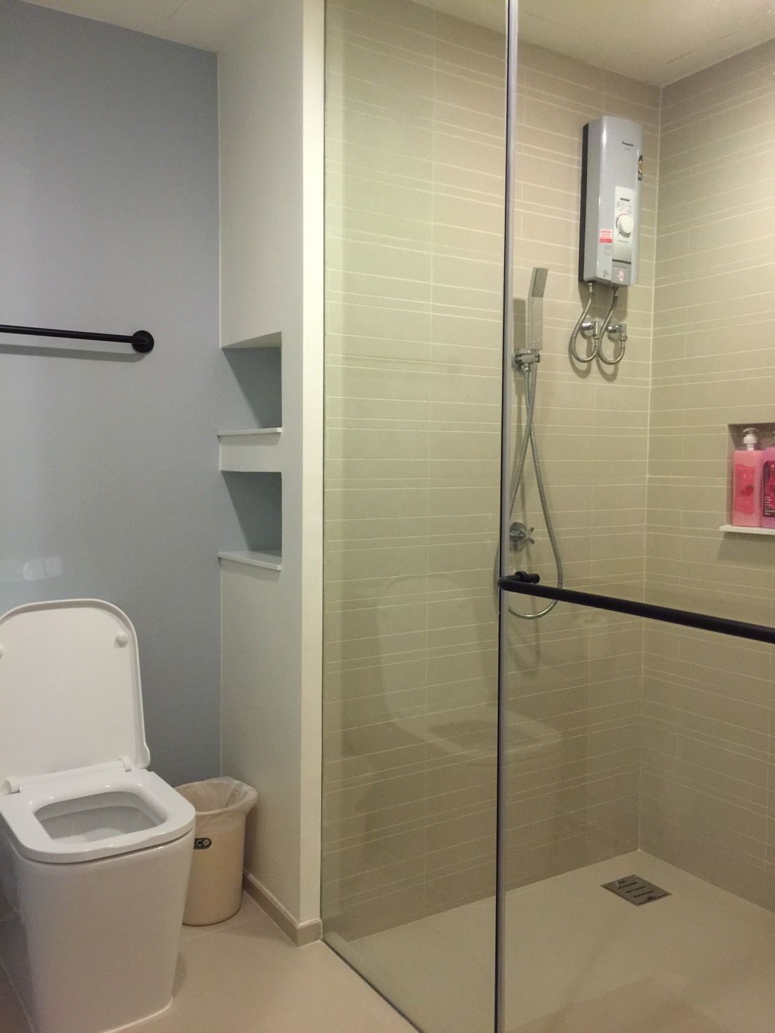 A modern bathroom with a glass-enclosed shower, a toilet, and a trash bin.