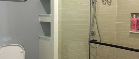 A modern bathroom with a glass-enclosed shower, a toilet, and a trash bin.