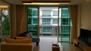A modern living room with a sofa, a coffee table, and a TV. There is a large sliding glass door leading to a balcony with a view of a building. - Luxury Wanvayla Condo (Hua Hin)